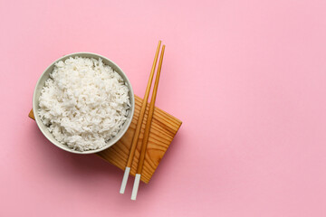 Bowl with tasty boiled rice and chopsticks on pink background