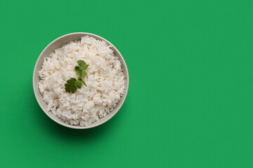 Bowl with tasty boiled rice on green background