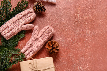 Warm gloves, fir branches and gift box on red background