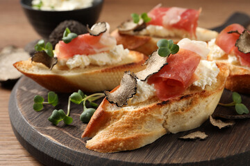 Delicious bruschettas with cheese, prosciutto and slices of black truffle on wooden table, closeup