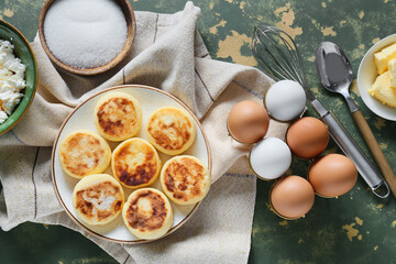 Plate with tasty cottage cheese pancakes and ingredients on grunge background