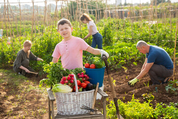 Portrait of smiling school boy engaged in gardening with family posing with freshly harvested...