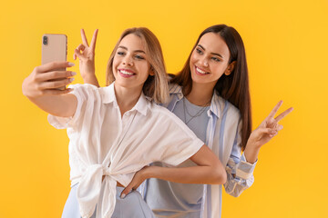 Young women with mobile phone taking selfie on yellow background