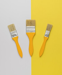 A set of paint brushes with yellow wooden handles on a white and yellow background. Trending color.