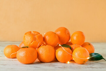 Tasty tangerines with Christmas lights on table