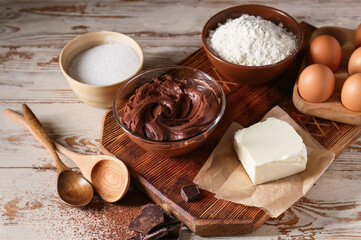 Bowl with fresh dough and ingredients for preparing chocolate brownie on white wooden background