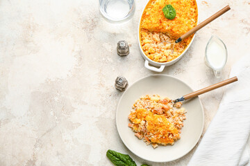 Plate and baking dish with tasty English fish pie on light background