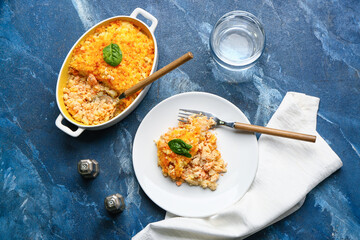 Plate and baking dish with tasty English fish pie on blue background