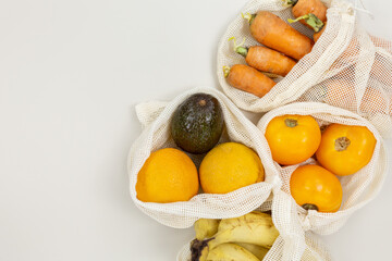 Fresh fruits, vegetables in eco cotton bags on beige table. Carrots, oranges, bananas, avocado from market. Zero waste shopping concept. Sustainable lifestyle with no plastic