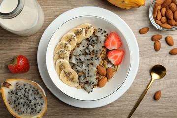 Bowl of granola with pitahaya, banana, almond and strawberry on wooden table, flat lay