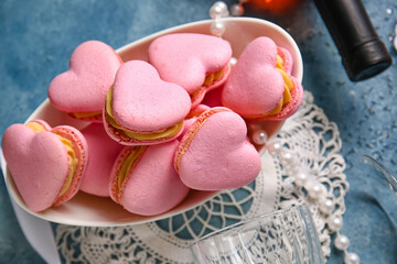 Bowl with tasty heart-shaped macaroons on blue background