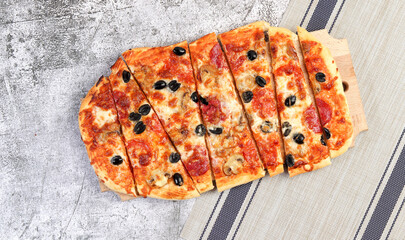 Sliced roman square pizza with cheese, sausage, mushrooms, olives and tomatoes on a square wooden cutting board on a dark gray background. Top view, flat lay