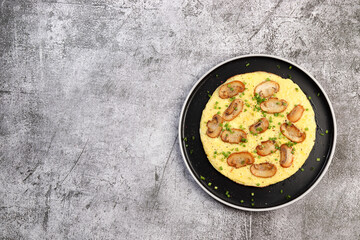 Omelet with mushrooms and green onions on a round plate on a dark gray background. Top view, flat lay
