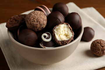 Bowl with many different delicious chocolate truffles on wooden table