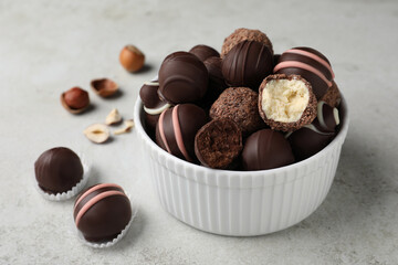 Different delicious chocolate truffles in bowl on light grey table