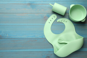 Flat lay composition with silicone baby bib and plastic dishware on light blue wooden background....