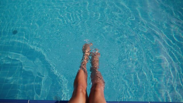 woman is swinging her legs in clear water of swimming pool, happy summer vacation