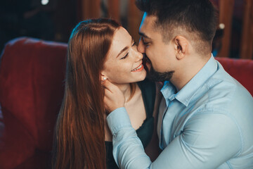 Close-up portrait of happy caucasian couple kissing and enjoying a good time together on valentine day on sofa. Couple celebrating Valentine's Day, Women's Day