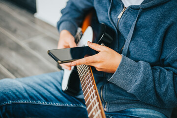 Persona viendo el celular mientras toca la guitarra electrica