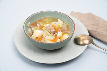 Meatball soup with vegetables in a light pastel bowl