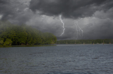 Lightnings in rainy clouds over forest and river