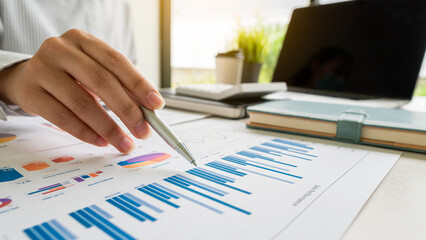 Businessman holding a profitability statistics analysis pen from a graph document in hand with a calculator and laptop on the table to plan profit growth from the past year.