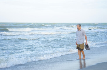senior man carrying shoes walking on the sand beach