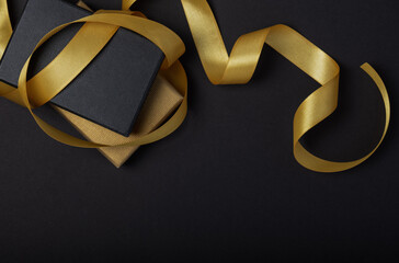 Black gift box with a golden ribbon  on a black  background. Place for the inscription
