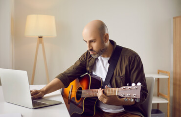 Serious focused beginner musician learning to play music on his instrument at home, looking at...