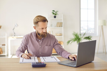 Serious businessman calculates company's internal accounts using laptop and calculator. Focused man...