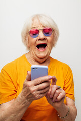 smiling elderly woman in fashionable glasses with a smartphone in hand light background