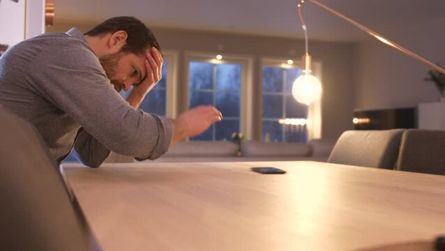Pensive Sad Man at kitchen table reads disappointing text Message on phone