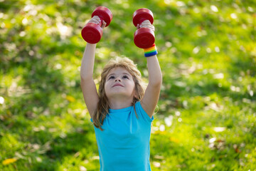 Healthy kid boy with dumbbell exercise outdoor. Little child practice dumbbells exercises in park. Funny excited child sportsman.