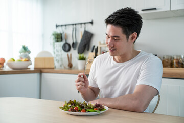 Asian attractive handsome male eating green salad in kitchen at home.