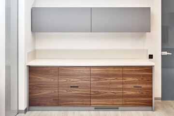 Fototapeta premium Contemporary kitchen furniture set in minimalist style of walnut wood and gray color with acrylic solid surface countertop in office