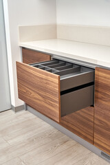 Open drawers of dark grey color with cutlery tray in contemporary kitchen of walnut wood and gray color with acrylic solid surface countertop close-up