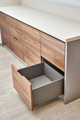 Open lower drawer of dark grey color in contemporary kitchen of walnut wood and gray color with...