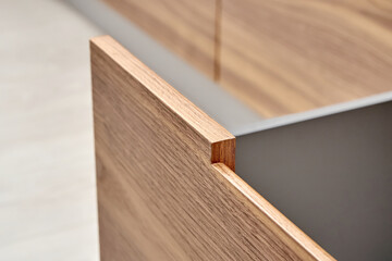 Open drawer of dark grey color with facade of walnut wood with finger pull design in contemporary...