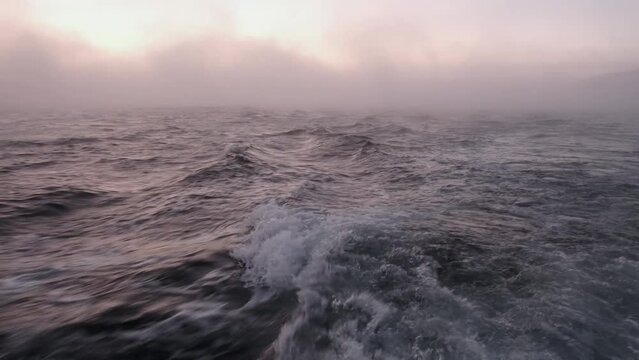 The texture of the seething blue sea salt water with waves, spills, bubbles, foam after a swiftly floating boat. Fast ship back view over Barents Sea surface in winter at sunset