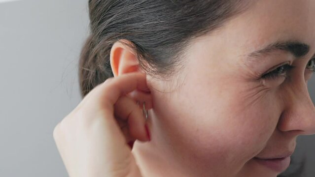 Close-up of the face of a young Caucasian woman scratching her ear with an earring and piercing inside with her finger. The concept of ear pain and deafness.