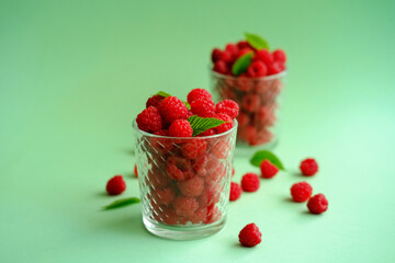 Fresh ripe raspberries in a glass on a green background