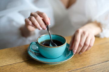 girl stirs sugar in a cup of coffee. Close-up of a hot drink mug with very shallow depth of field.