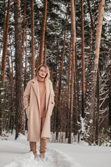 Mid age woman in winter forest outdoors looking at camera. Girl in coat and sweater full length shot.