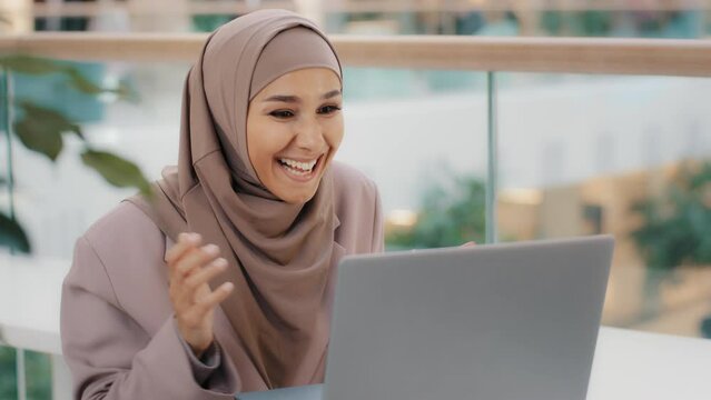 Happy young arab woman sitting at desk receiving email on laptop with good news shocked excited girl rejoices in victory making yes gesture winning achievement credit approval hired great exam result