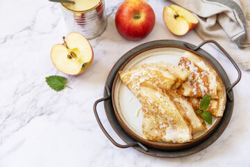 Celebrating Pancake day, healthy breakfast. Homemade sweet crepes with apples and condensed milk on a marble tabletop. Copy space.