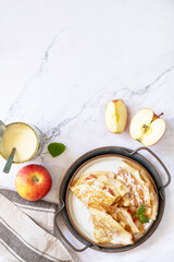 Celebrating Pancake day, healthy breakfast. Homemade sweet crepes with apples and condensed milk on a marble tabletop.  Top view flat lay. Copy space.