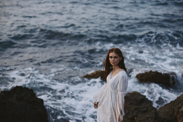 Woman in white dress stands on a cliff lifestyle stone coast landscape