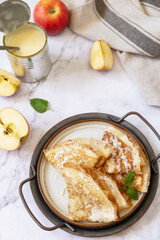 Celebrating Pancake day, healthy breakfast. Homemade sweet crepes with apples and condensed milk on a marble tabletop.