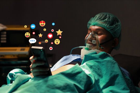 Happy funny asian patient man lying in bed and using internet on smart mobile phone with social media interaction, notification icons, wow, love, and message above device at hospital emergency room. - Powered by Adobe