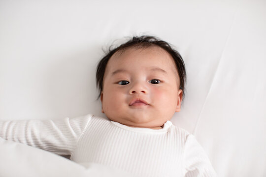 Top view happy newborn baby lying on a white bed and blanket comfortable and safety.Cute Asian newborn looking around on bed.Newborn Baby Care concept